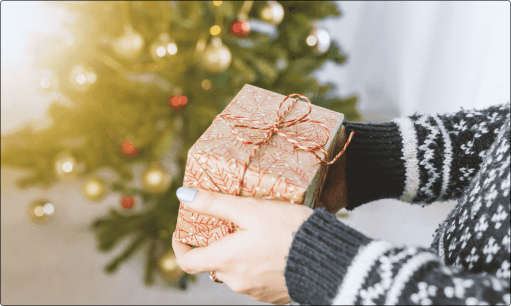 person giving someone a packaged gift with a christmas tree in the background.